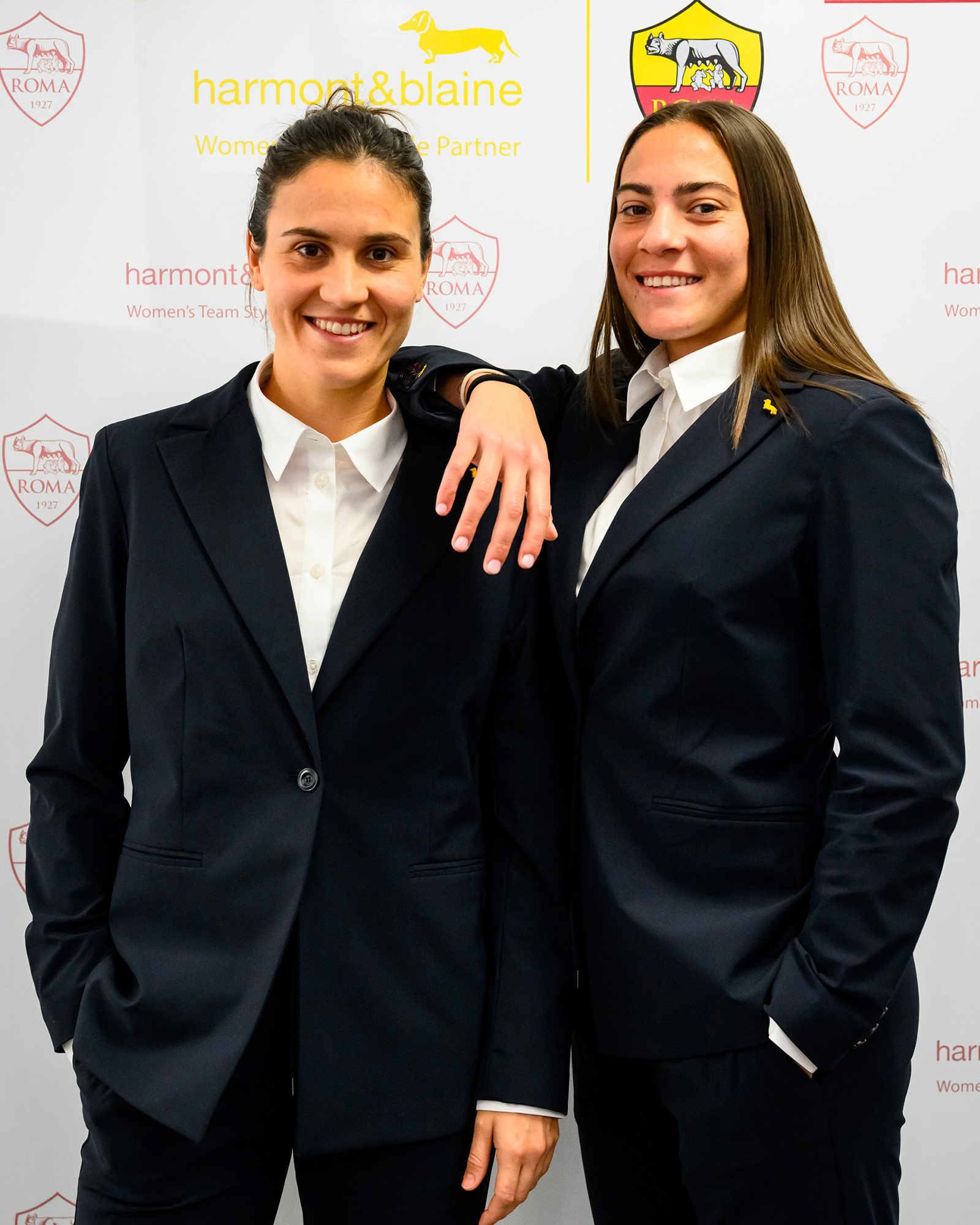 Two women wearing navy blue suits with white shirts.
