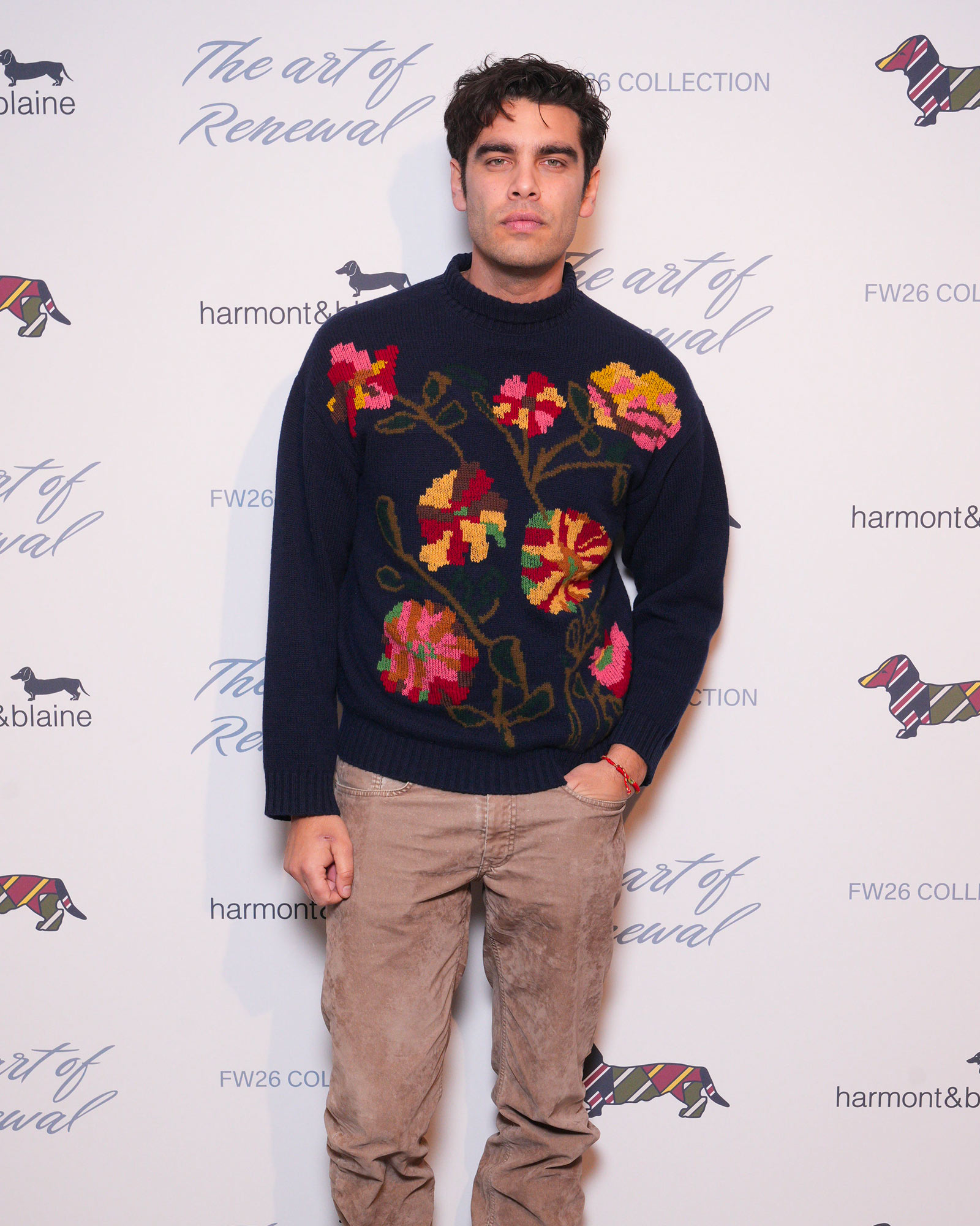 Man wearing navy sweater with floral embroidery and beige trousers