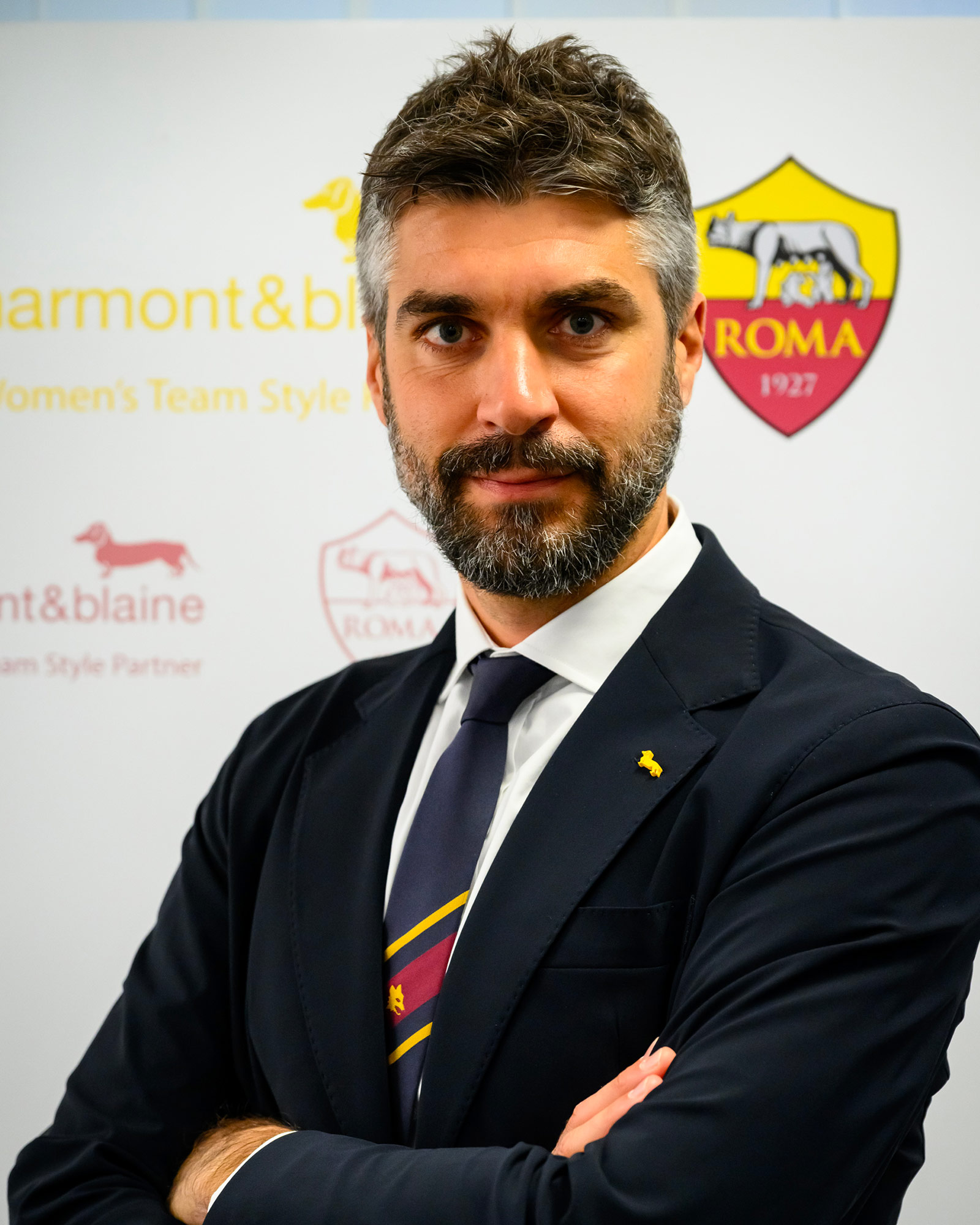 Man wearing a navy blue suit with striped tie and yellow pin.