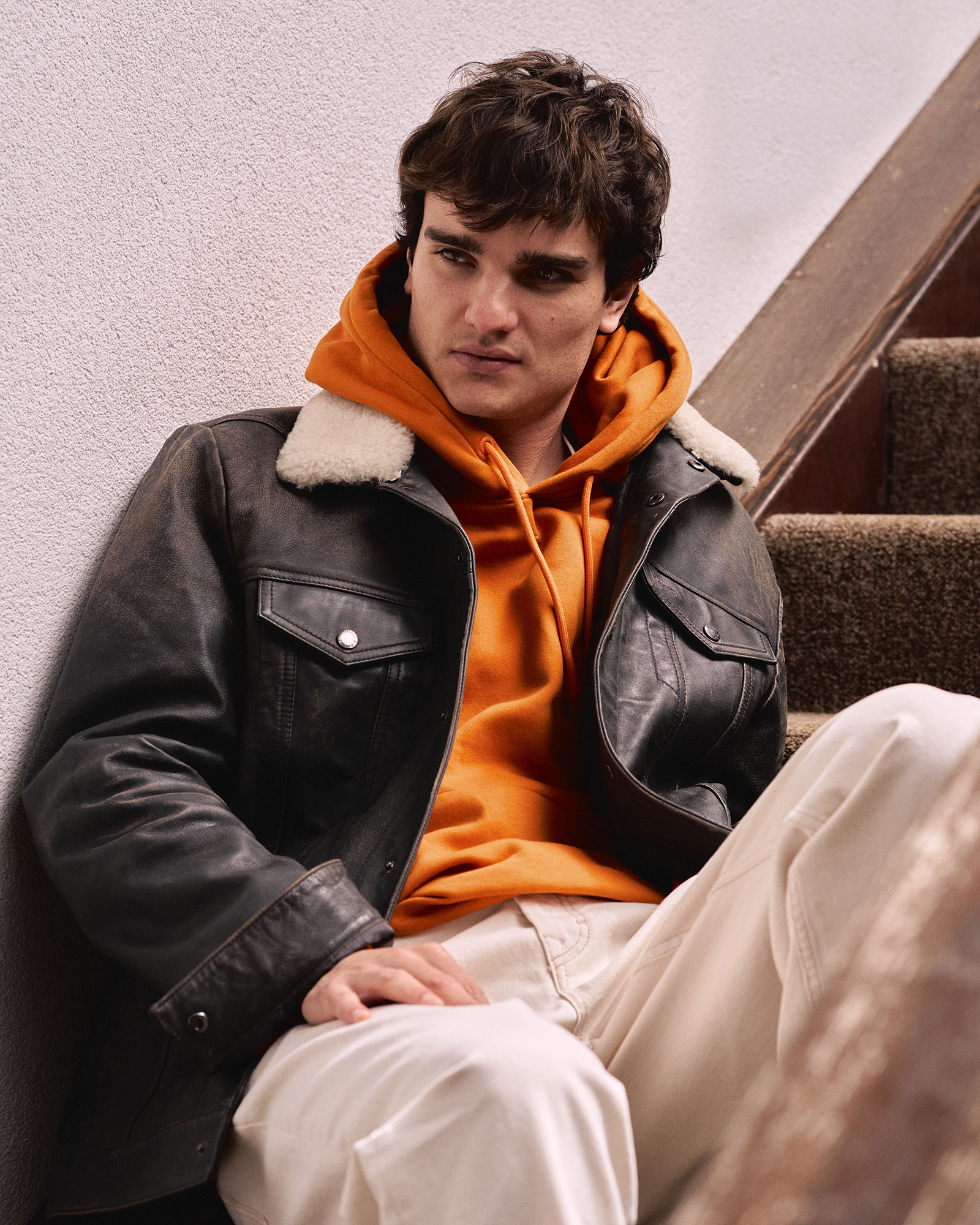 Model wearing leather jacket and orange hoodie.