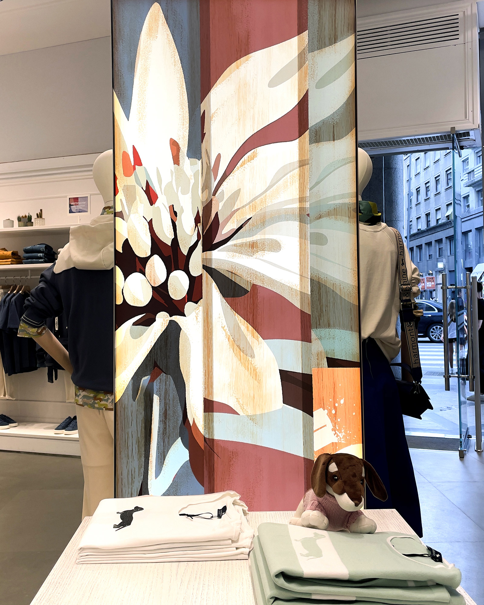 Harmont & Blaine FW25 window with large stylized flower and denim and casual outfits.