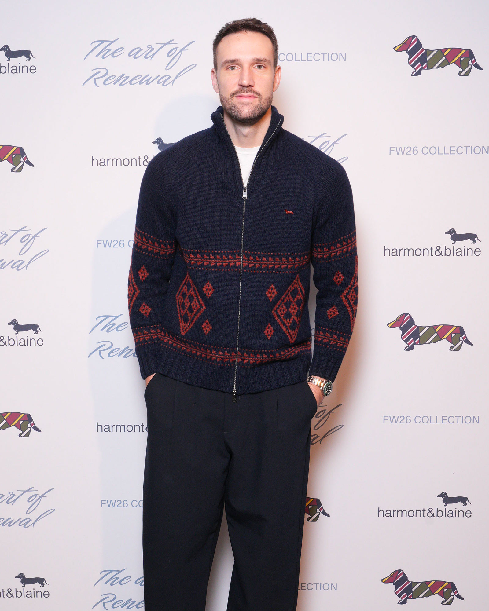 Man wearing navy sweater with red geometric patterns and dark trousers
