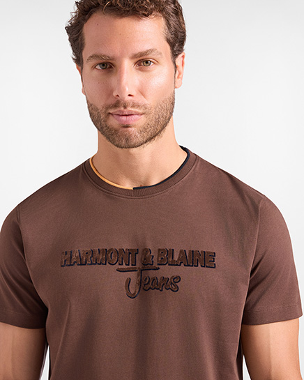 For the HB Jeans t-shirts category, a model wears a dark brown short-sleeved t-shirt featuring a crew neck with a contrasting trim detail and the "HARMONT & BLAINE Jeans" logo embroidered on the chest against a white background.