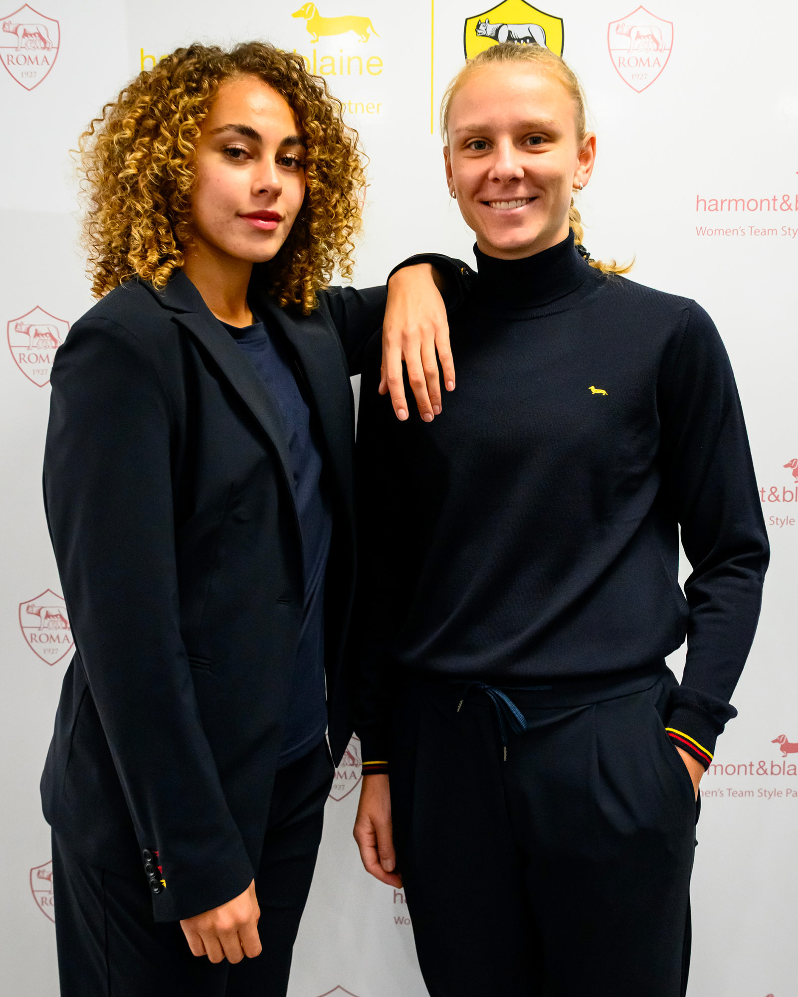 Two women in navy blue uniforms, one in a turtleneck and the other in a blazer.