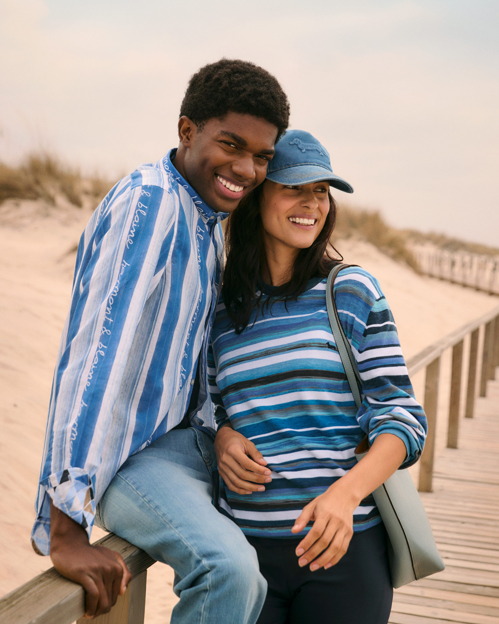Pareja en la playa con polos de rayas y gorras de b&eacute;isbol